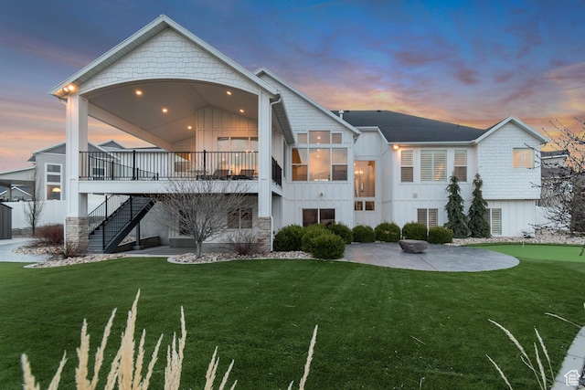 back of property at dusk featuring a patio area, a yard, board and batten siding, and stairs