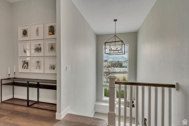 stairs featuring baseboards, wood finished floors, a notable chandelier, and plenty of natural light
