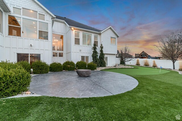 back of house at dusk featuring a patio, a yard, board and batten siding, and fence