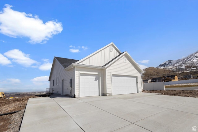 view of home's exterior with board and batten siding, a garage, fence, a mountain view, and concrete driveway