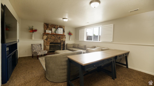 carpeted living area featuring baseboards, visible vents, a stone fireplace, and a textured ceiling