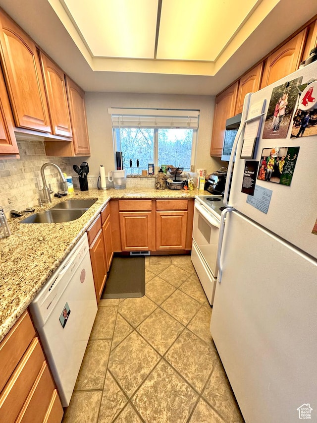 kitchen with tasteful backsplash, light stone counters, white appliances, a raised ceiling, and a sink