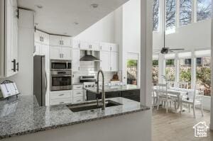 827 E 1070 S, St George, UT 84790 - kitchen with wall chimney range hood, white cabinets, light stone countertops, stainless steel appliances, and a sink