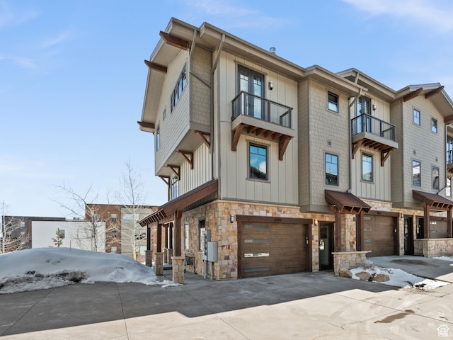 multi unit property with stone siding, a garage, board and batten siding, a balcony, and driveway