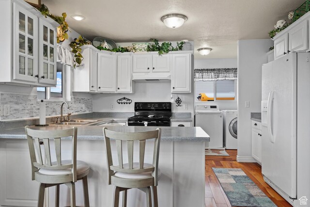 kitchen featuring a sink, a peninsula, black gas range, white refrigerator with ice dispenser, and washing machine and dryer