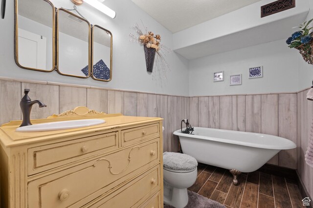 bathroom with wood finish floors, a freestanding tub, vanity, a wainscoted wall, and toilet