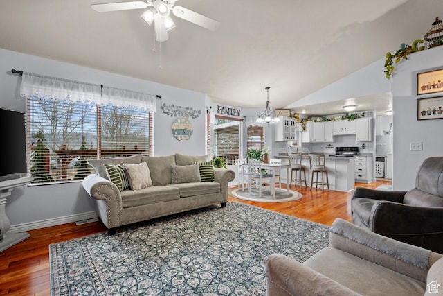 living area featuring baseboards, light wood finished floors, vaulted ceiling, and ceiling fan with notable chandelier