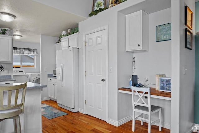 kitchen featuring washer and dryer, light wood-type flooring, white fridge with ice dispenser, and white cabinetry