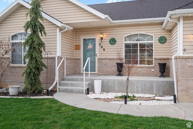 property entrance featuring a yard, a shingled roof, and brick siding