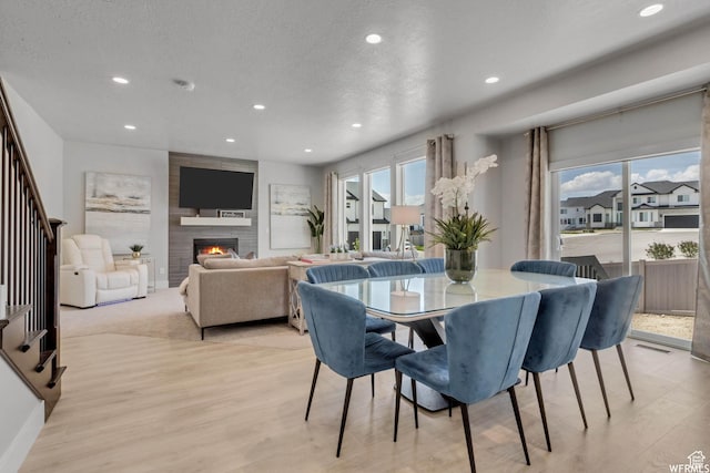 dining space with light wood-style flooring, recessed lighting, a large fireplace, and stairway