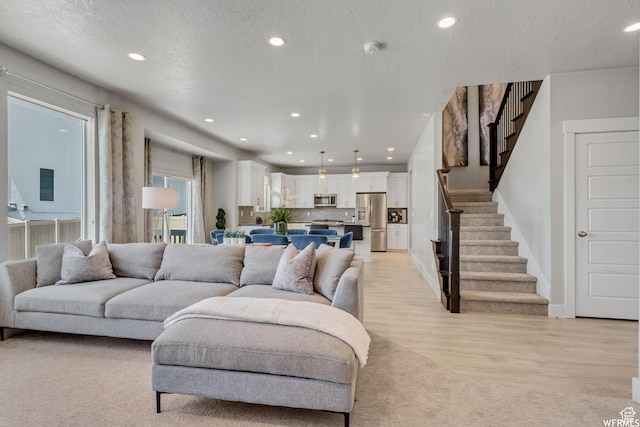 living area with a textured ceiling, light wood-style flooring, recessed lighting, and stairs
