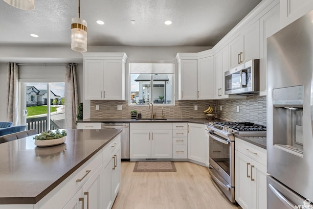 kitchen featuring a sink, light wood-style flooring, dark countertops, and stainless steel appliances