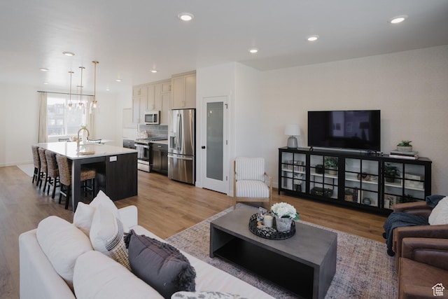 living area featuring baseboards, light wood-type flooring, a notable chandelier, and recessed lighting