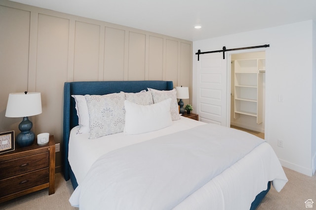 bedroom featuring a decorative wall, a spacious closet, a barn door, and light carpet
