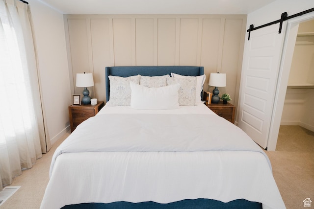bedroom with a decorative wall, visible vents, a barn door, and light carpet