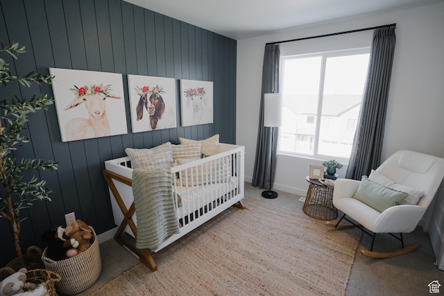 carpeted bedroom featuring wood walls, baseboards, and a nursery area