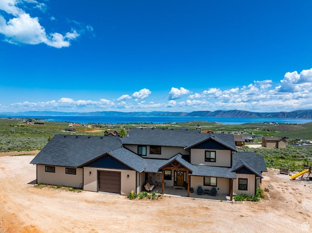 3525 S Sweetwater Pkwy, Garden City, UT 84028 - view of front of house with an attached garage, a mountain view, a shingled roof, covered porch, and dirt driveway