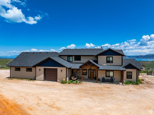 3525 S Sweetwater Pkwy, Garden City, UT 84028 - view of front of house featuring a garage, roof with shingles, dirt driveway, covered porch, and a mountain view