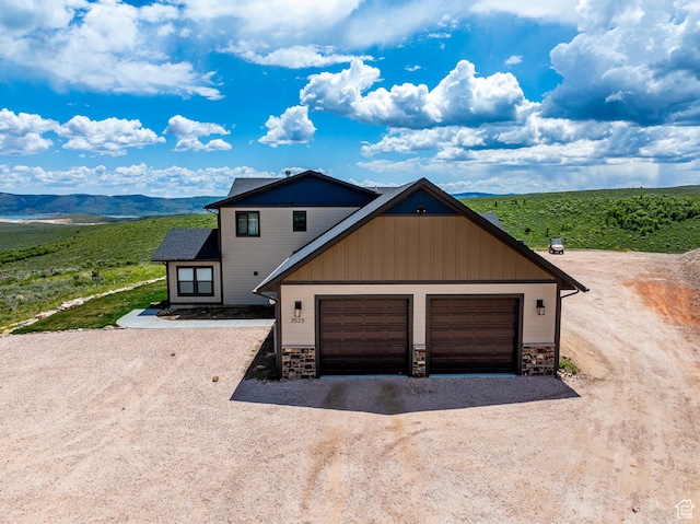 3525 S Sweetwater Pkwy, Garden City, UT 84028 - view of front facade with stone siding, dirt driveway, board and batten siding, a garage, and a mountain view