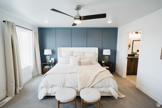 bedroom featuring a decorative wall, ceiling fan, light colored carpet, and baseboards