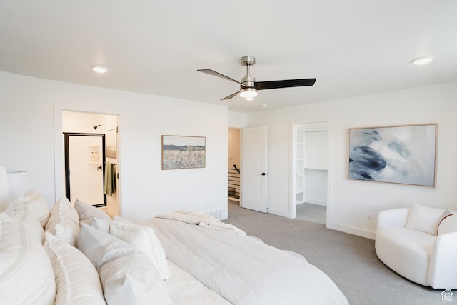 bedroom featuring baseboards, a spacious closet, ensuite bath, a ceiling fan, and light colored carpet