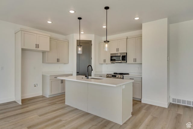 kitchen featuring a sink, a center island with sink, light countertops, appliances with stainless steel finishes, and visible vents