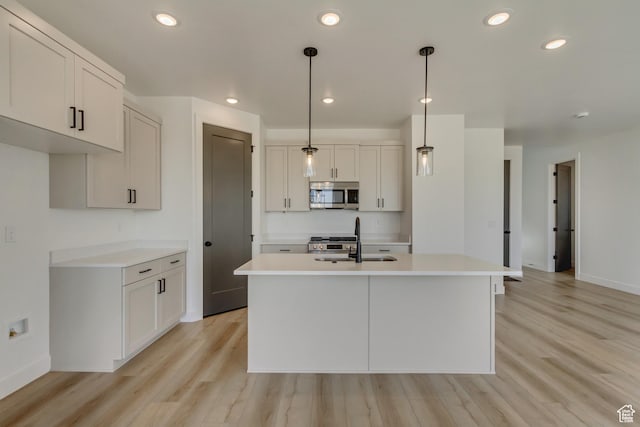 kitchen featuring light wood-type flooring, appliances with stainless steel finishes, a kitchen island with sink, light countertops, and a sink