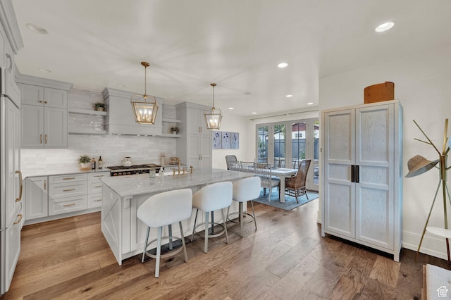 kitchen featuring a breakfast bar, light wood-type flooring, backsplash, open shelves, and a kitchen island with sink