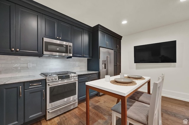 kitchen featuring tasteful backsplash, wood finished floors, light stone counters, and stainless steel appliances