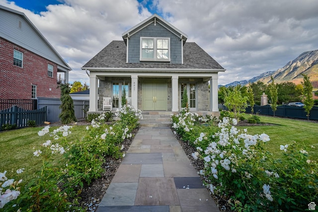 bungalow featuring a front yard, a mountain view, covered porch, fence, and roof with shingles