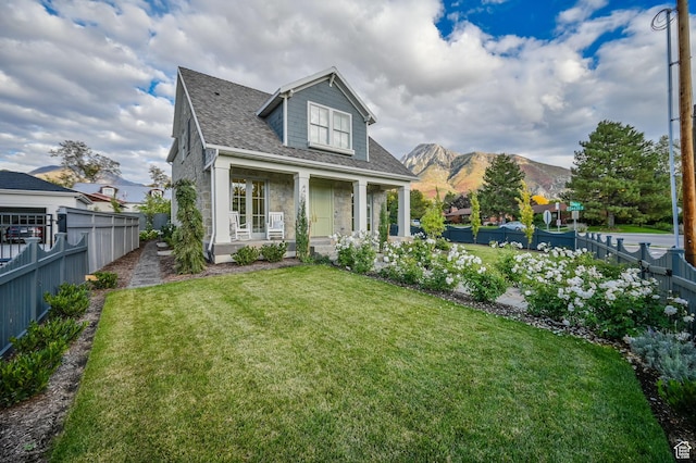 view of front facade with a front yard, a fenced backyard, a porch, and a mountain view