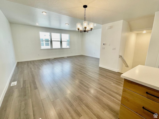 unfurnished dining area featuring a chandelier, visible vents, baseboards, and wood finished floors