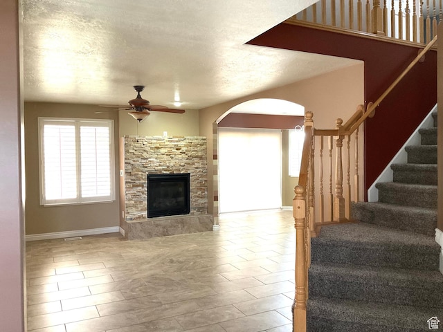 2461 N 2710 W, Clinton, UT 84015 - living room with arched walkways, ceiling fan, a stone fireplace, stairway, and a textured ceiling