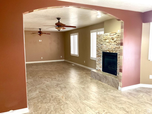 2461 N 2710 W, Clinton, UT 84015 - unfurnished living room with a ceiling fan, a fireplace, arched walkways, and baseboards