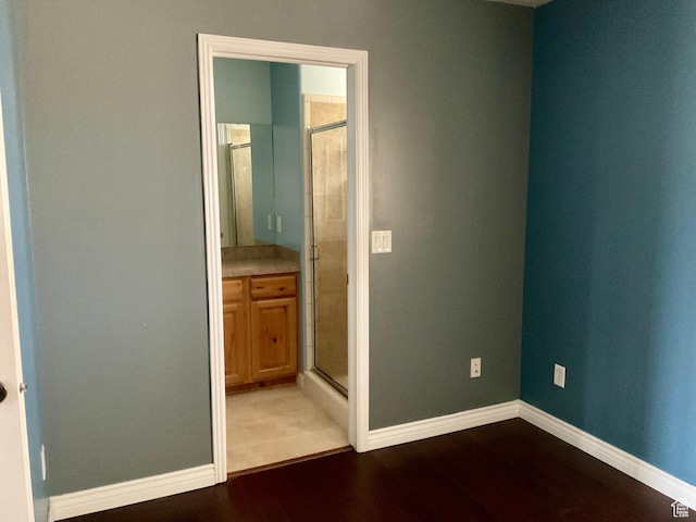 unfurnished bedroom with dark wood-style flooring, baseboards, and connected bathroom