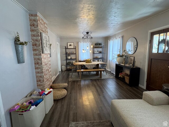 living room featuring crown molding, a textured ceiling, a chandelier, dark wood-style flooring, and baseboards