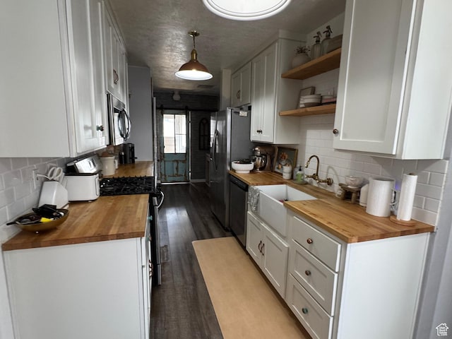 kitchen with dishwashing machine, open shelves, stainless steel microwave, a sink, and wooden counters