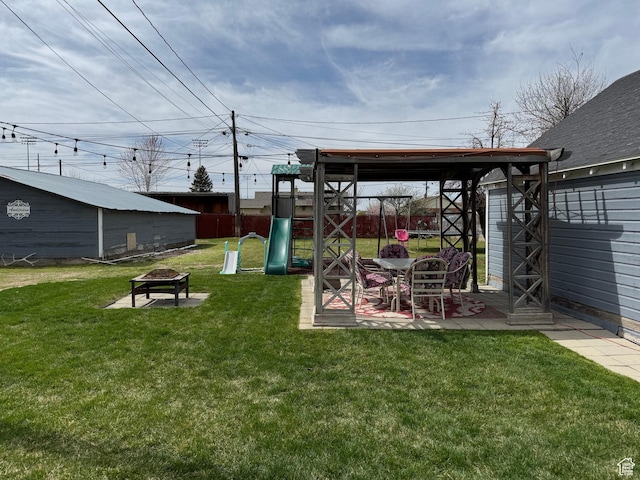 view of yard with a fire pit, fence, a playground, a patio, and an outbuilding