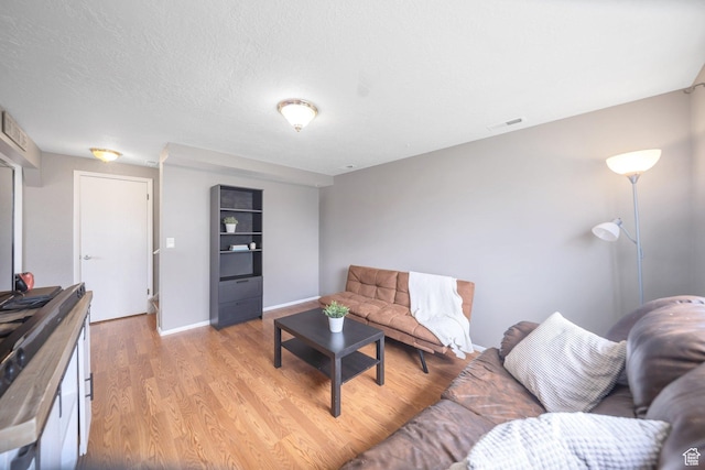 living area featuring a textured ceiling, light wood finished floors, baseboards, and visible vents