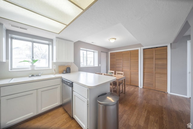 kitchen with a peninsula, white cabinets, dishwasher, light countertops, and a sink
