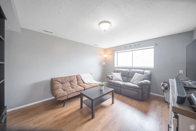 living room with a textured ceiling, wood finished floors, baseboards, and visible vents