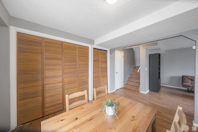 unfurnished dining area with stairs, baseboards, a textured ceiling, and wood finished floors
