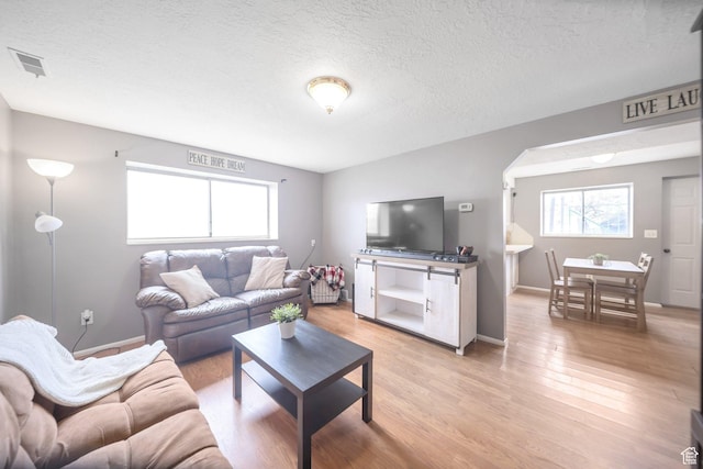 living area with plenty of natural light, light wood finished floors, visible vents, and a textured ceiling