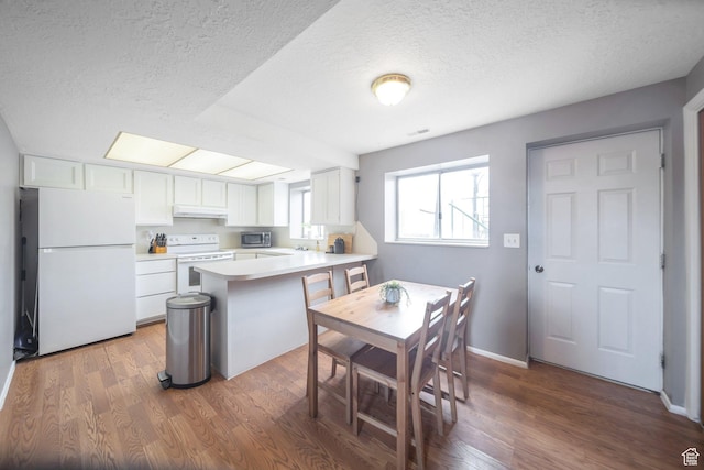 kitchen featuring white appliances, a peninsula, white cabinetry, under cabinet range hood, and visible vents