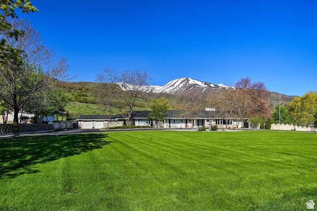 back of property featuring an attached garage, driveway, a mountain view, and a lawn
