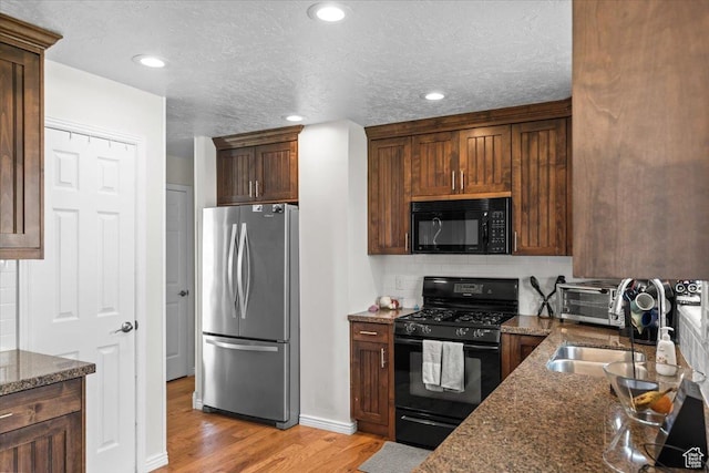 kitchen featuring a textured ceiling, black appliances, dark stone countertops, light wood finished floors, and decorative backsplash