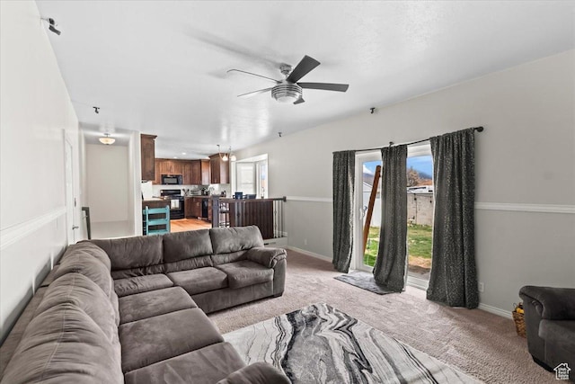 living area featuring baseboards, a ceiling fan, and light colored carpet