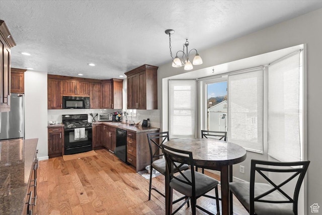kitchen with dark stone counters, light wood-type flooring, black appliances, a sink, and decorative backsplash