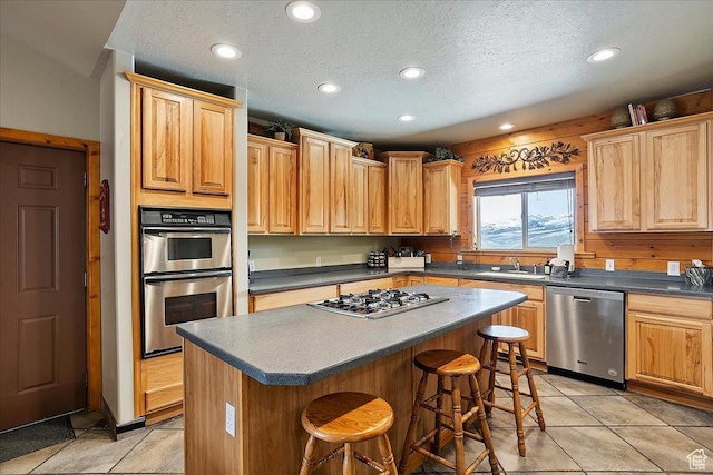 kitchen featuring a sink, dark countertops, stainless steel appliances, a kitchen island, and a breakfast bar area