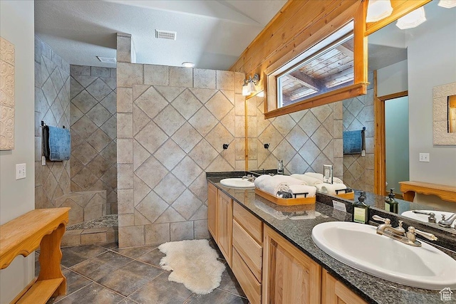 bathroom featuring visible vents, a sink, tile walls, a walk in shower, and double vanity
